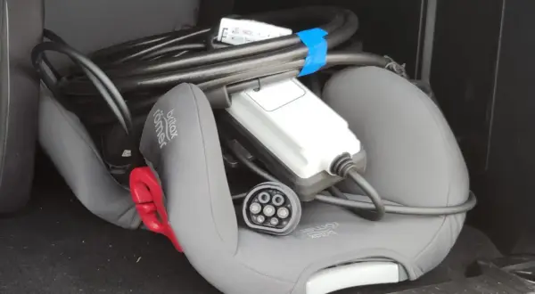 Kabel do ładowania samochodów elektrycznych leży na foteliku dziecięcym w bagażniku.