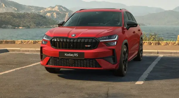 Czerwony Skoda Kodiaq RS zaparkowany nad jeziorem, z górami w tle.