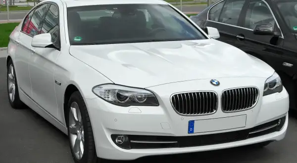 Białe BMW 535d z chromowanymi detalami i przyciemnianymi szybami, zaparkowane obok czarnego samochodu.