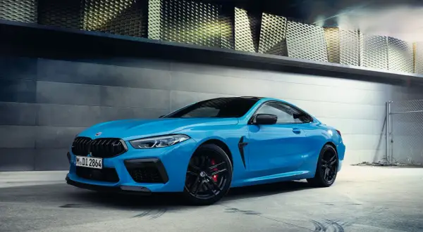 Niebieskie BMW M8 Coupe na tle nowoczesnej architektury.
