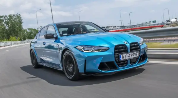 Niebieskie BMW M3 Competition pędzi po drodze, błyszcząc w słońcu.