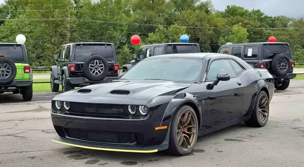 Czarny Dodge Challenger SRT z żółtym akcentem na zderzaku. Obok inne samochody i balony. Sprawdź dodge challenger cena!