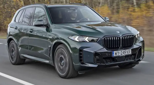 Zielony BMW X5 M50d pędzi po drodze, otoczony jesiennym lasem.