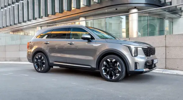 Elegancki, szary Kia Sorento 2025 z czarnymi felgami stoi przed nowoczesnym budynkiem.