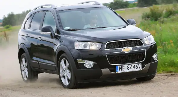Czarny Chevrolet Captiva z kierowcą w okularach przeciwsłonecznych jedzie po piaszczystej drodze, wzbijając kurz.