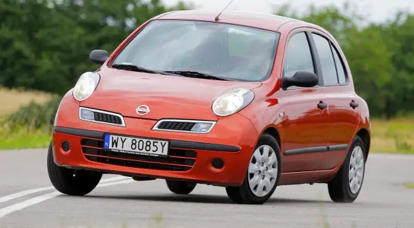 Pomarańczowy Nissan Micra K12 na drodze, z zielenią w tle.