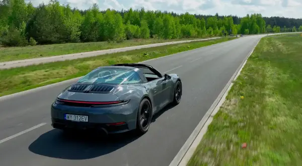Szary Porsche Targa sunie po asfaltowej drodze, otoczony zielenią.