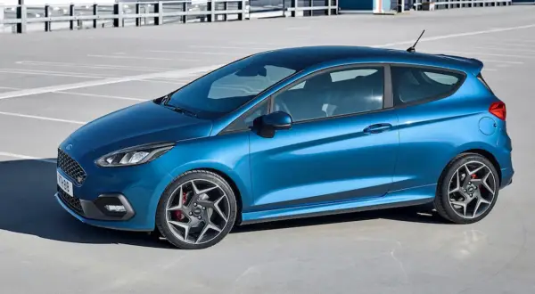 Niebieski Ford Fiesta ST z czarnym dachem i felgami stoi na parkingu.