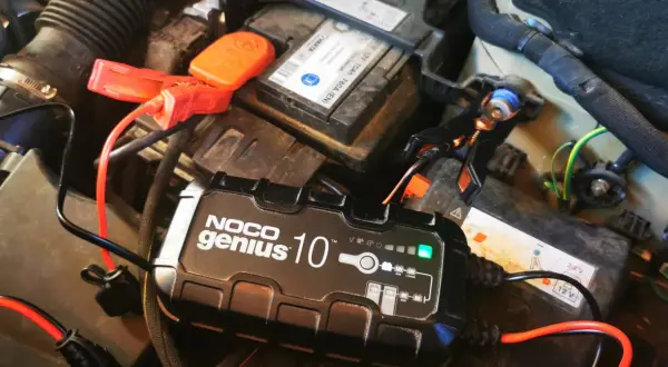 Ładowarka NOCO Genius 10 podłączona do akumulatora samochodowego, rozpoczyna proces odsiarczania akumulatora.