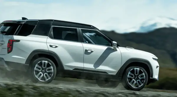 Biały SUV torres auto pokonuje wyboistą drogę, wzbijając tumany kurzu. W tle górzysty, surowy krajobraz.