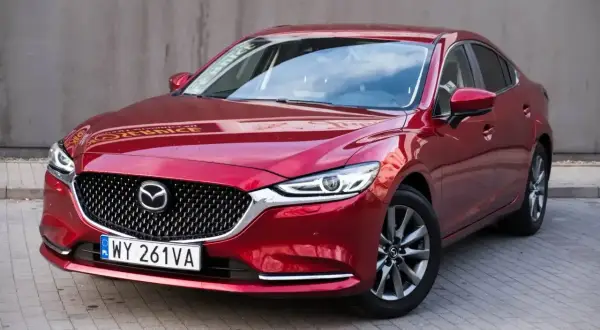 Czerwona Mazda 6 2.0 benzyna z eleganckim grillem i nowoczesnymi światłami, zaparkowana na kostce brukowej.