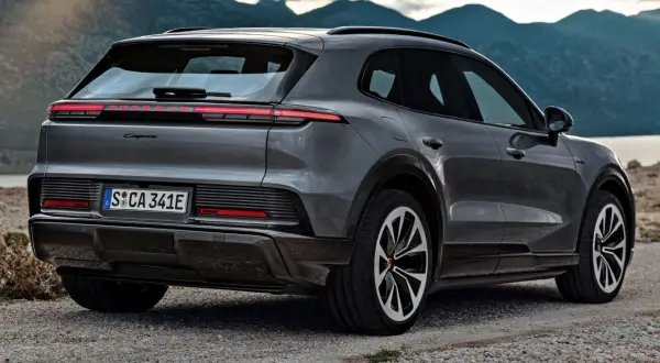 Nowe Porsche Cayenne w szarym kolorze, zaparkowane na kamienistej drodze z widokiem na góry i jezioro.