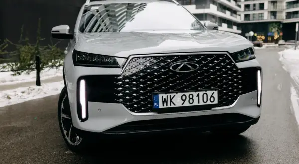 Biały Tiggo 4 z charakterystycznym grillem i pionowymi światłami LED, zaparkowany na mokrej drodze.