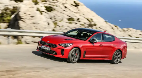 Czerwony Kia Stinger pędzi po krętej drodze nad morzem.