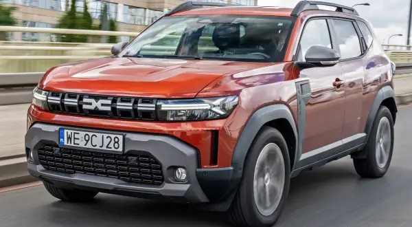 Pomarańczowy Renault Duster jedzie po drodze, z nowoczesnym designem i wyraźnym logo.