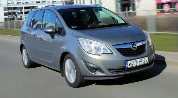 Szary Opel Meriva B w ruchu miejskim, z widocznym kierowcą za kierownicą.
