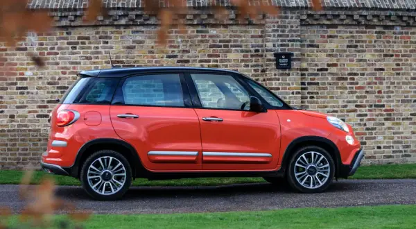 Pomarańczowy Fiat 500 XL z czarnym dachem zaparkowany przy ceglanej ścianie.