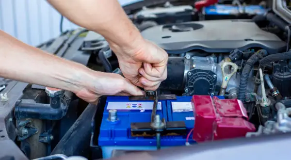Ręce mechanika dokręcają klemę akumulatora. Widać silnik i elementy instalacji elektrycznej, czuć napięcie przed uruchomieniem.