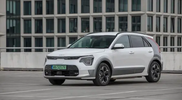 Biała Kia Niro na parkingu, z nowoczesnym budynkiem w tle. Sprawdź kia niro wymiary, by poznać jej kompaktową sylwetkę.