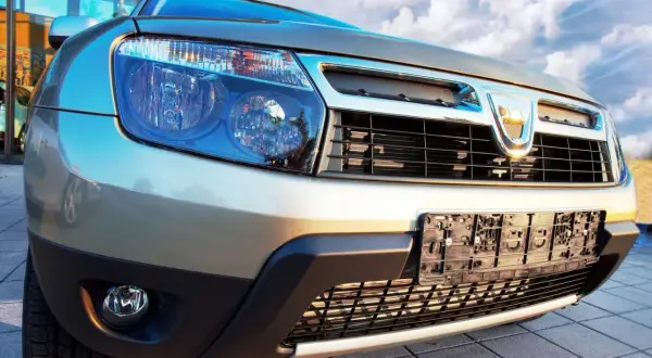 Złoty Dacia Duster 1.6 benzyna z bliska, z widocznym grillem i reflektorami.