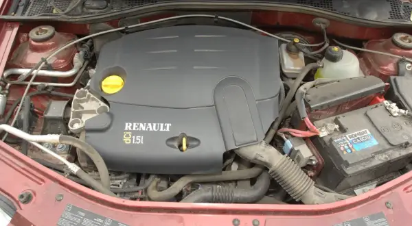 Silnik Renault 1.5 dCi w samochodzie Dacia. Widoczny jest czarny plastikowy dekiel silnika z napisem RENAULT 1.5 dCi, akumulator i elementy układu chłodzenia.