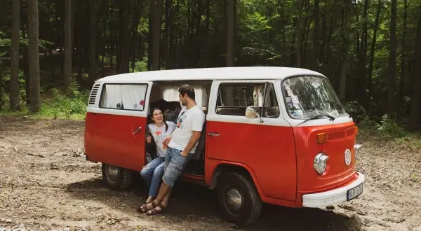 Para zakochanych odpoczywa przy swoim czerwono-białym vw t2 w lesie.