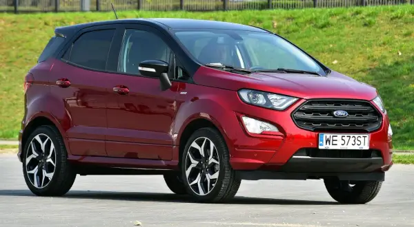 Czerwony Ford EcoSport z czarnym dachem, zaparkowany na tle zielonego zbocza.