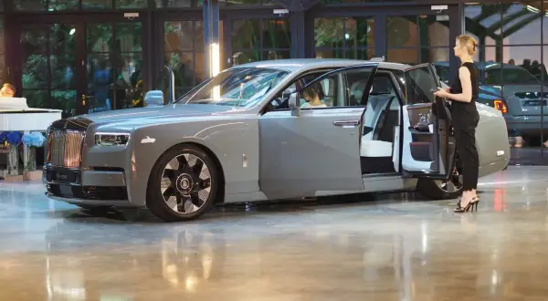Elegancki szary Rolls-Royce Phantom z otwartymi drzwiami, obok stoi kobieta. Poznaj jego imponującą rolls royce cena.