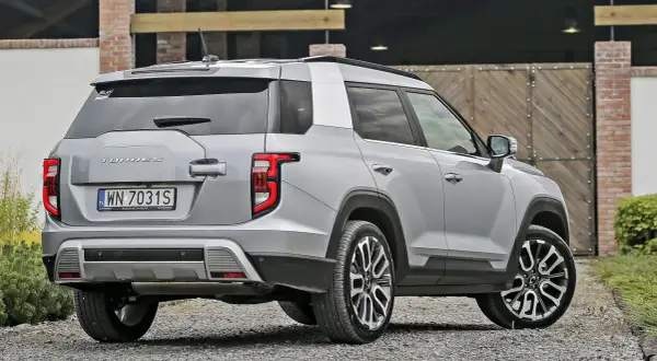 Srebrny SsangYong Torres z polskimi tablicami rejestracyjnymi WN 7031S stoi na żwirowej drodze przed drewnianą bramą.