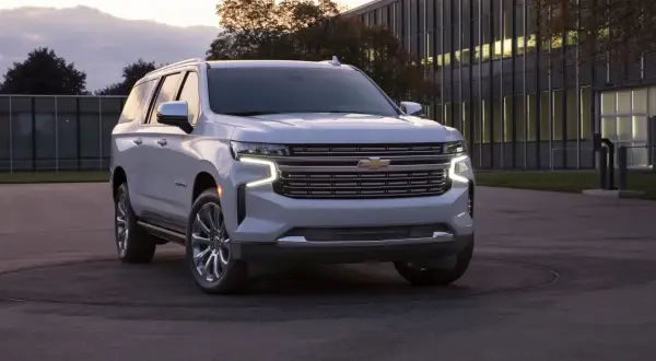Biały Chevrolet Suburban zaparkowany przed nowoczesnym budynkiem.