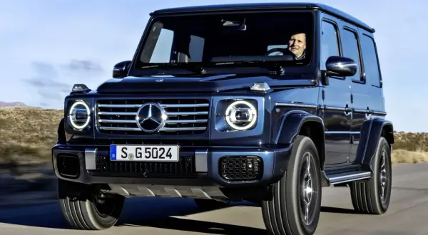 Ciemnoniebieski Mercedes G Klasa w ruchu. Kierowca uśmiecha się. Sprawdź aktualną mercedes g klasa cena.