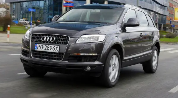 Ciemny Audi Q7 3.0 TDI w ruchu miejskim, z widocznym polskim numerem rejestracyjnym PO 2896X.