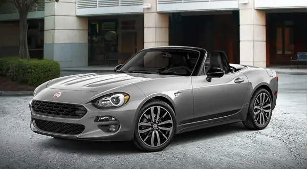 Szary Fiat Spider z czarnym dachem, zaparkowany przed budynkiem.