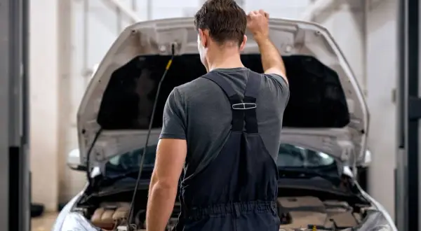 Mechanik zamyka maskę samochodu. Zastanawia się, ile czasu stygnie silnik, zanim będzie mógł kontynuować pracę.