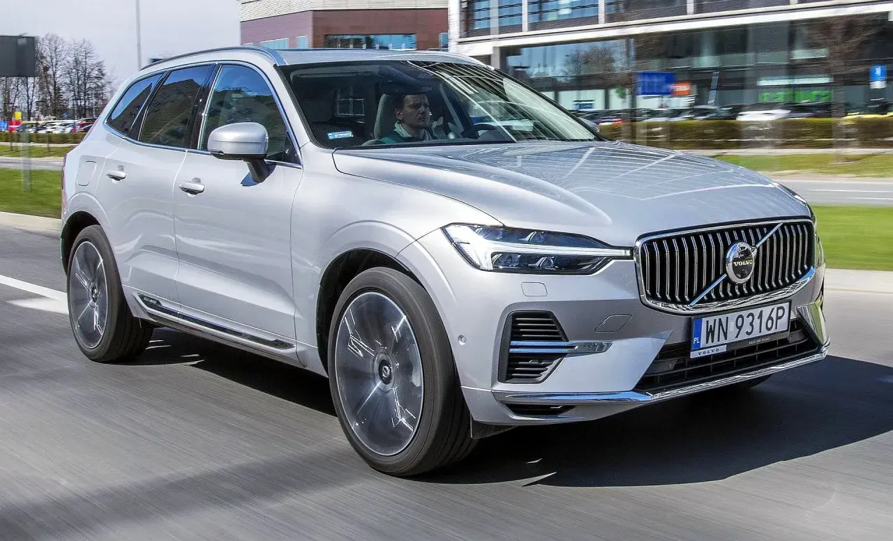 Srebrny Volvo XC60 T6 w ruchu miejskim, z kierowcą za kierownicą. Elegancki SUV na tle nowoczesnych budynków.