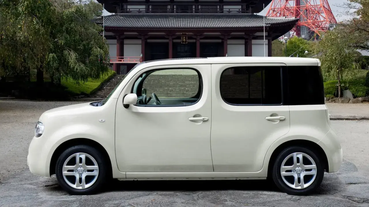 Biały Nissan Cube zaparkowany przed tradycyjną japońską świątynią.