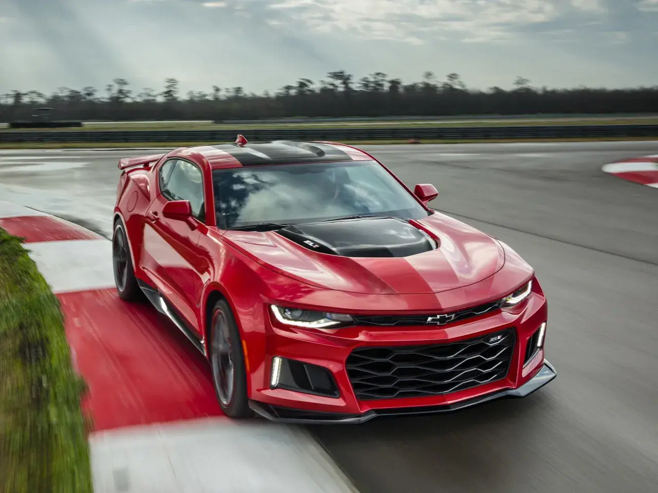 Czerwone Camaro ZL1 z czarnymi pasami pędzi po torze wyścigowym, zostawiając za sobą smugę prędkości.