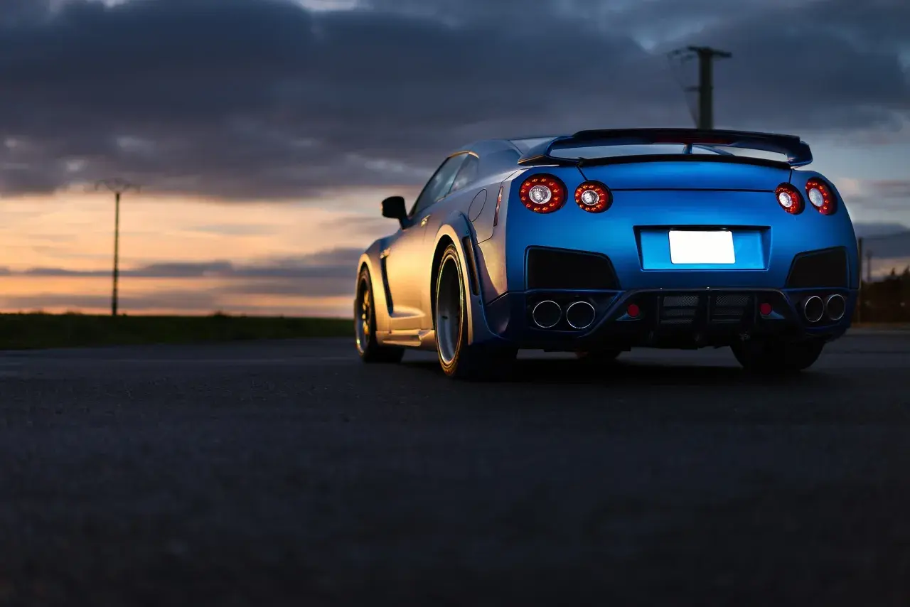 Niebieski Nissan GTR z charakterystycznymi światłami z tyłu, zaparkowany o zachodzie słońca. Zastanawiasz się nad nissan gtr cena?