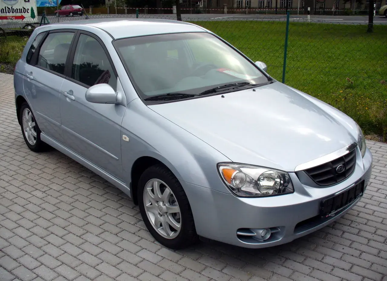 Jasnosrebrny Kia Cerato hatchback stoi na chodniku z kostki brukowej.