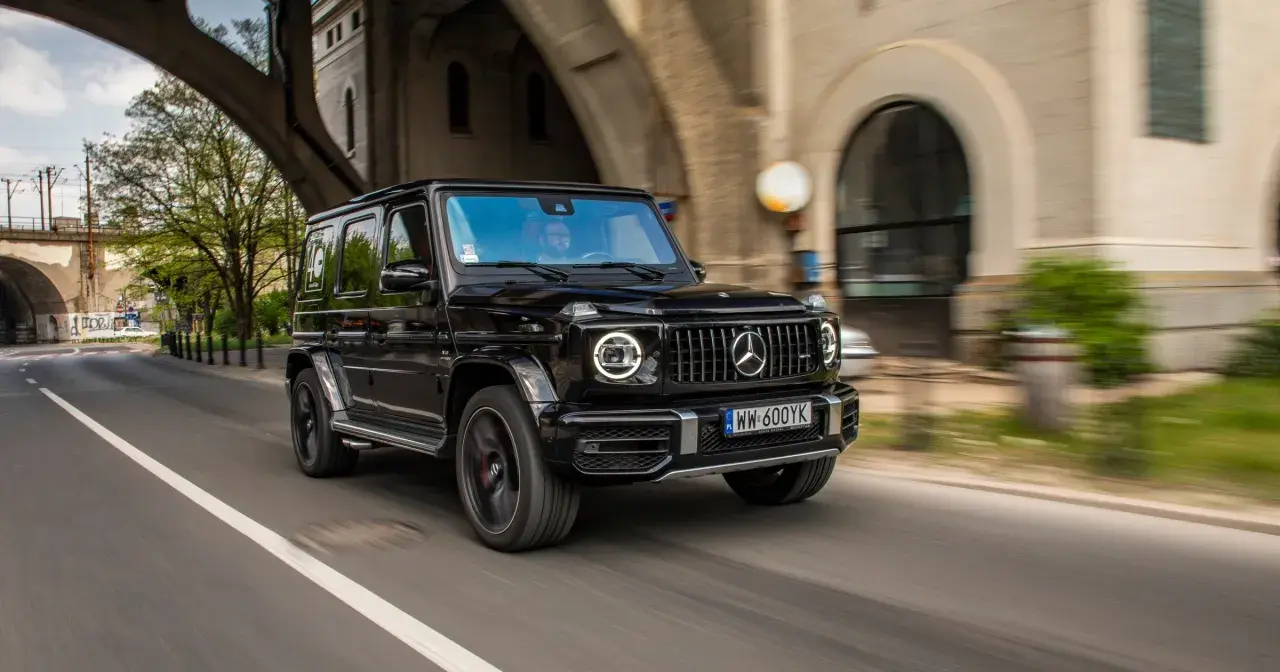 Czarny G-wagon pędzi pod wiaduktem, kierowca w okularach obserwuje drogę.