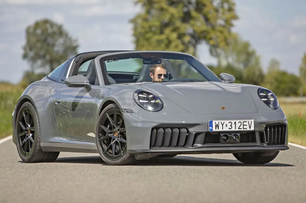 Szary Porsche 911 Targa z otwartym dachem, kierowca w okularach przeciwsłonecznych. Sprawdź porsche 911 cena!