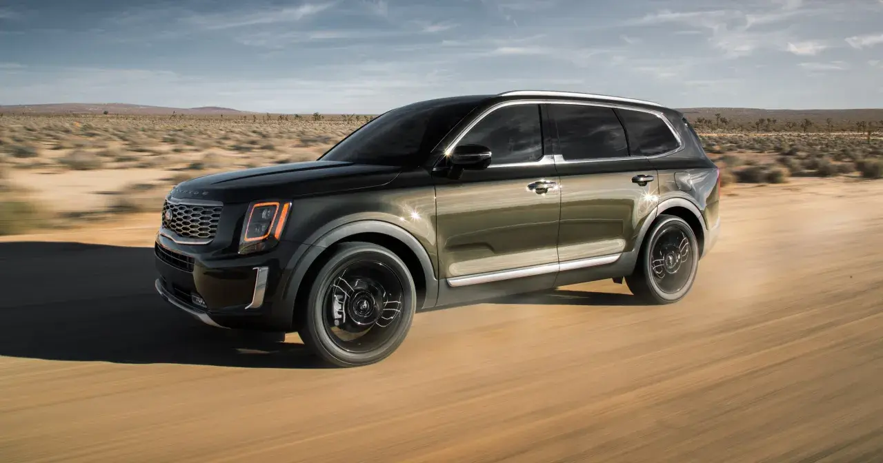 Ciemnozielony Kia Telluride przemierza pustynną drogę, unosząc kurz.