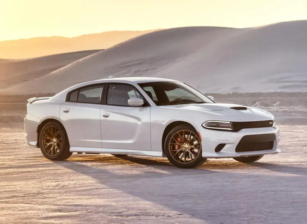 Biały Dodge Charger SRT z brązowymi felgami na pustyni o zachodzie słońca.