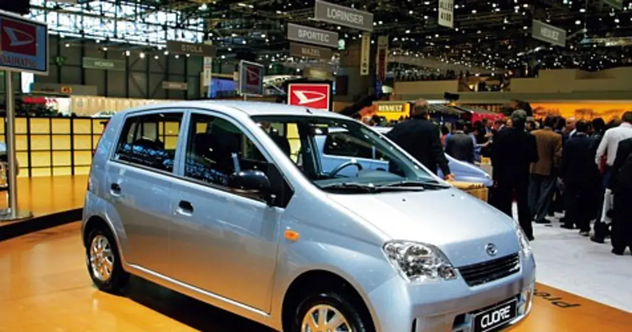 Srebrny Daihatsu Cuore na targach motoryzacyjnych, wśród tłumu ludzi i innych stoisk.