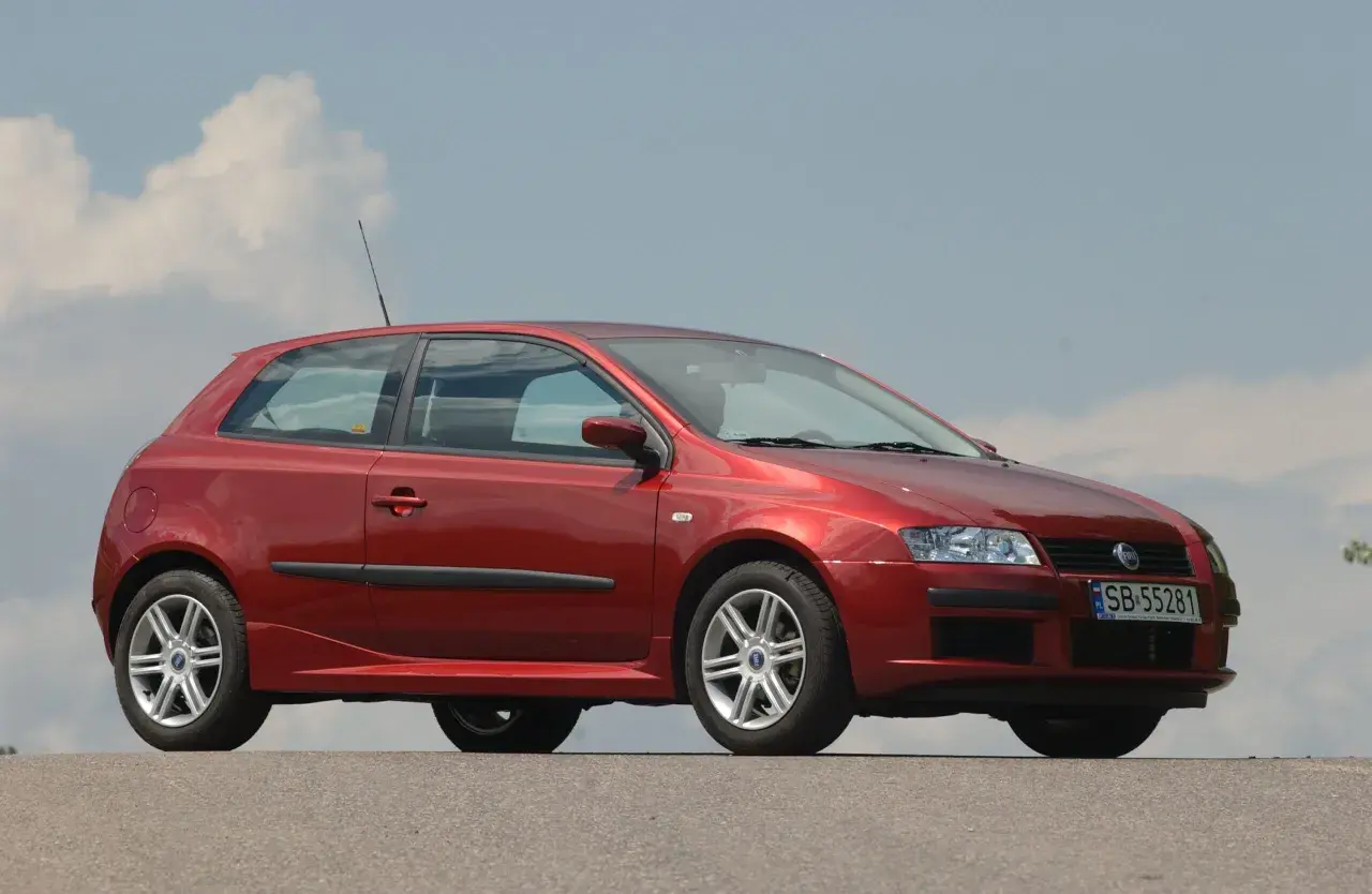 Czerwony Fiat Stilo 1.9 JTD z felgami aluminiowymi stoi na tle błękitnego nieba z chmurami.
