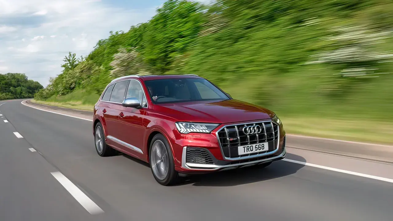 Czerwony Audi SQ7 pędzi po krętej drodze, otoczony zielenią.