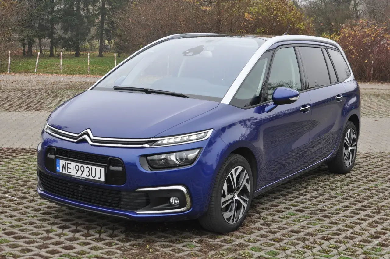 Niebieski Citroen C4 Spacetourer zaparkowany na betonowej nawierzchni z trawą.