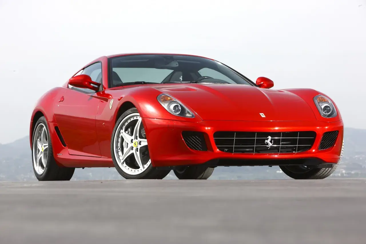Czerwone Ferrari 599, błyszczące w słońcu, z charakterystycznym grillem i felgami. Marzenie każdego miłośnika motoryzacji.