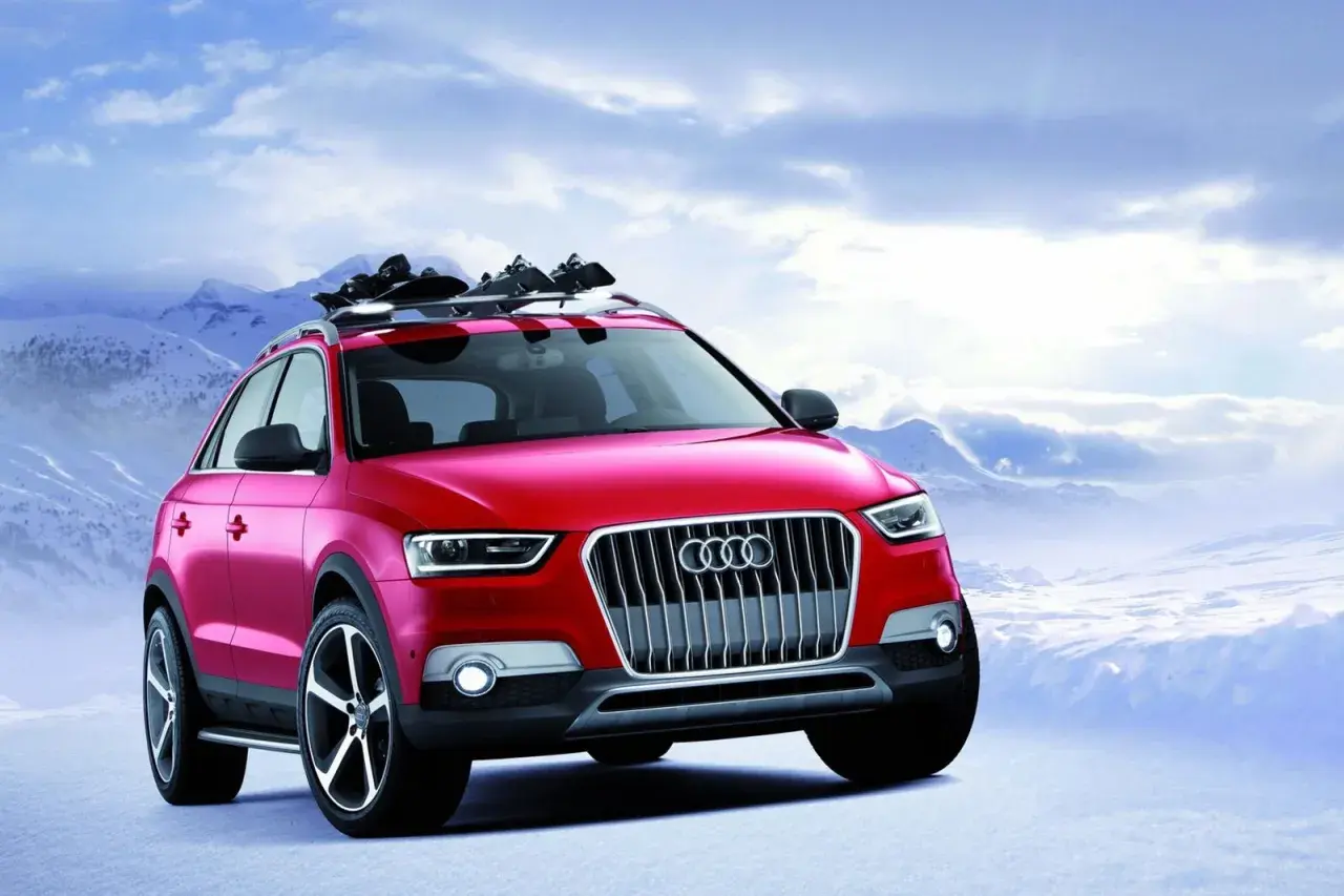 Czerwony Audi Q1 z nartami na dachu gotowy na zimową przygodę w górach.
