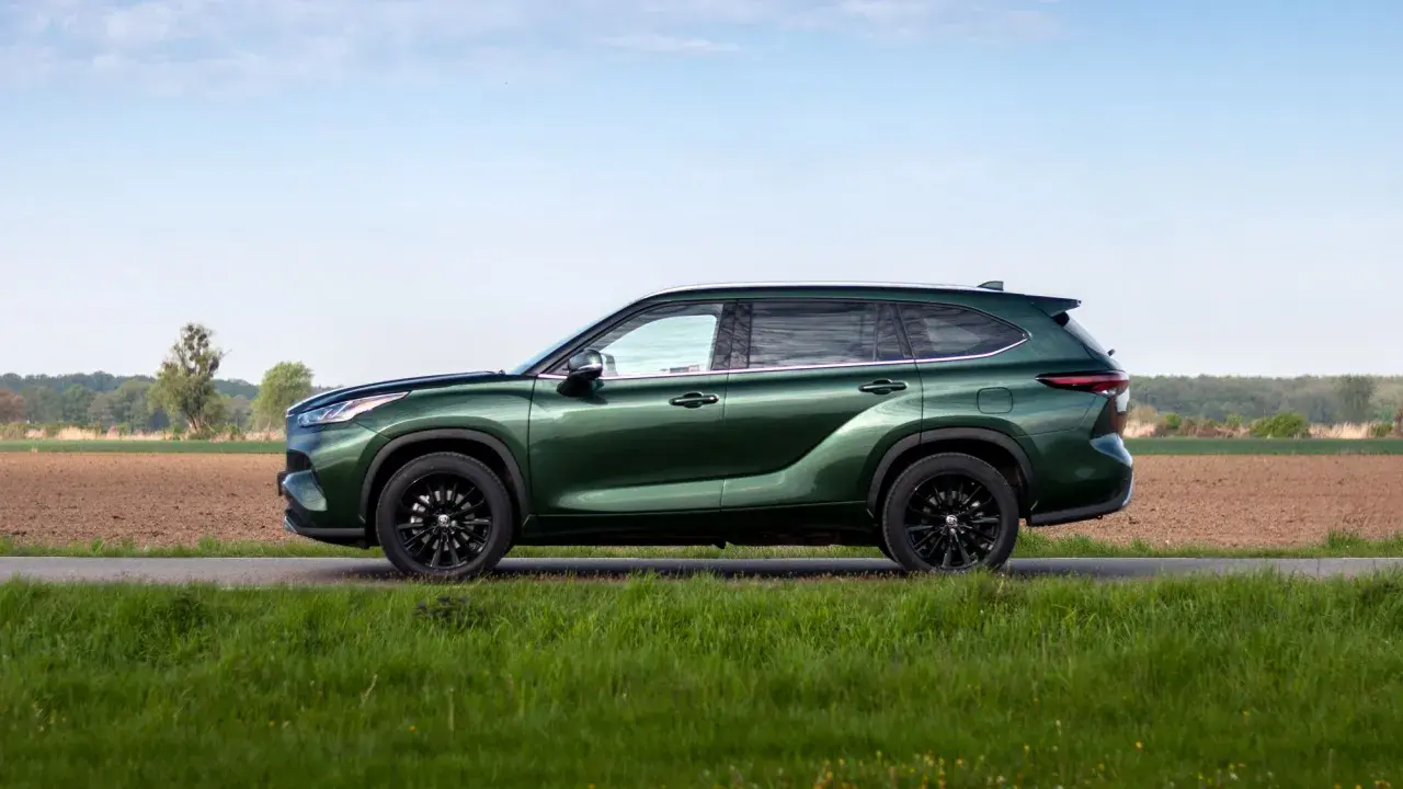 Zielony Toyota Grand Highlander z czarnymi felgami na tle pól i nieba.